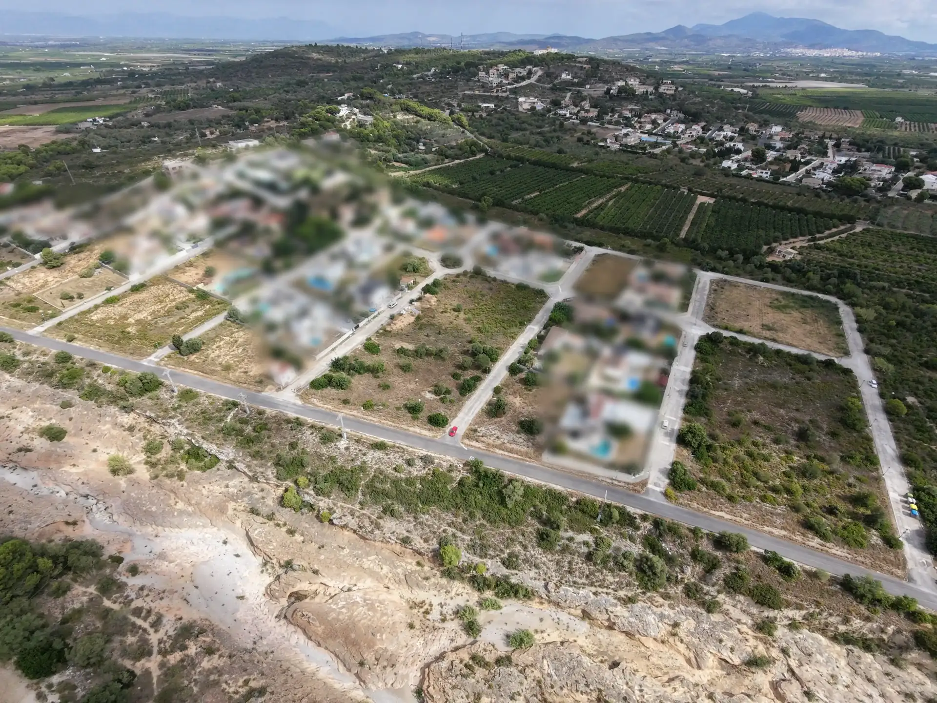 Vista aérea de El Puig de la Ermita en Vinaròs: viviendas unifamiliares, calles urbanizadas y parcelas edificables, con campos de cultivo y la sierra al fondo